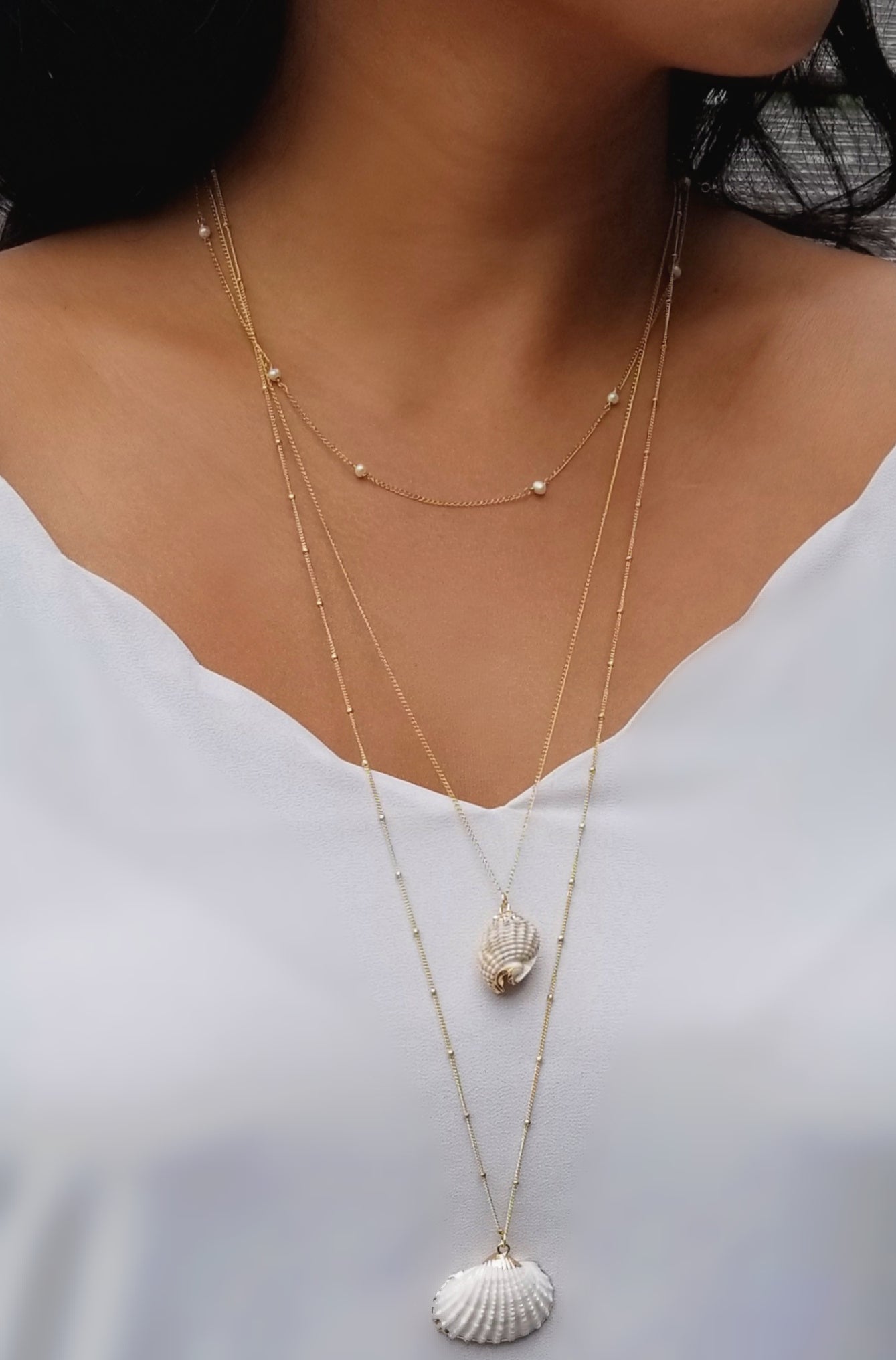 model wearing gold freshwater pearl strand layered with the clamshell and the conch gold necklace