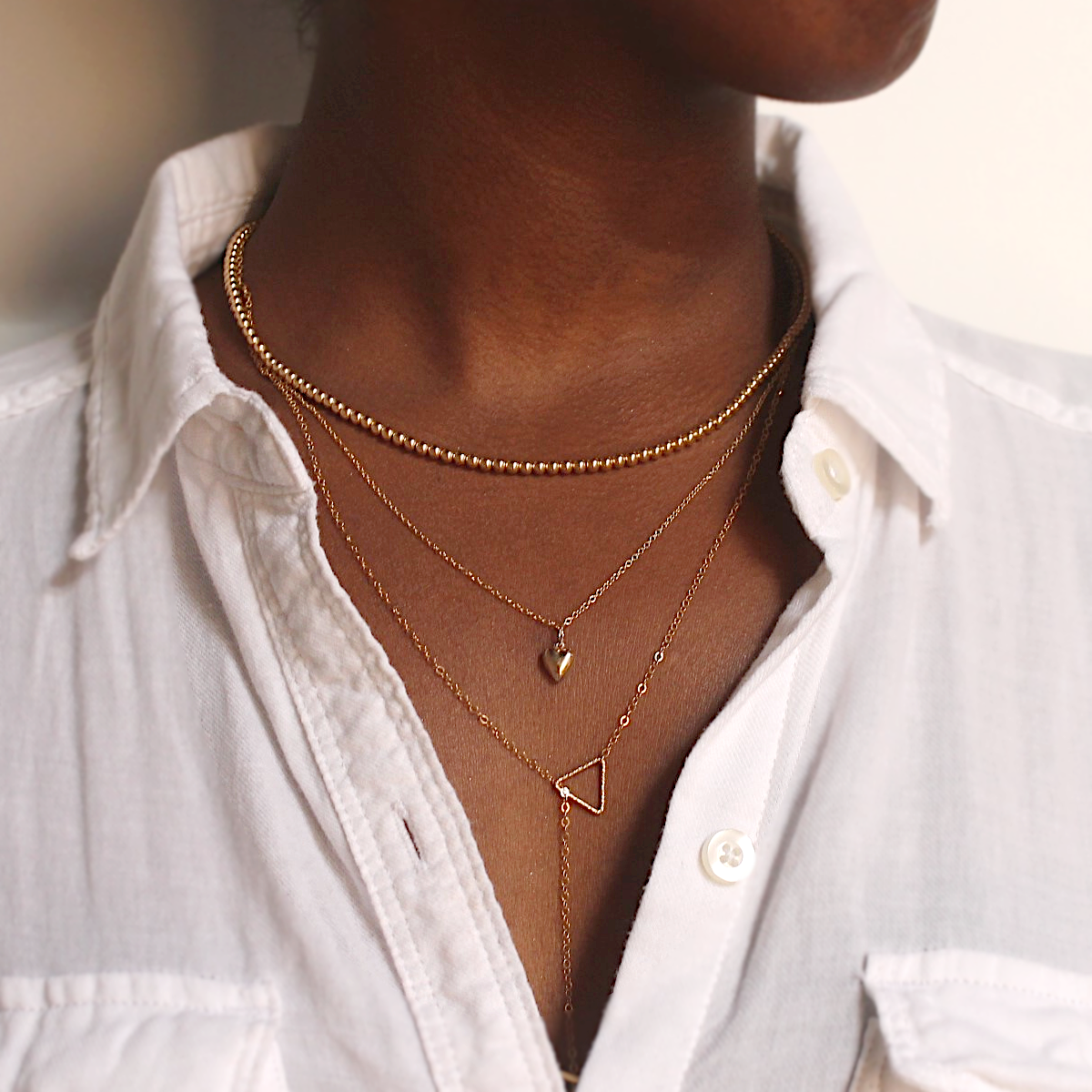 Model wearing gold beaded necklace, heart necklace and lariat necklace