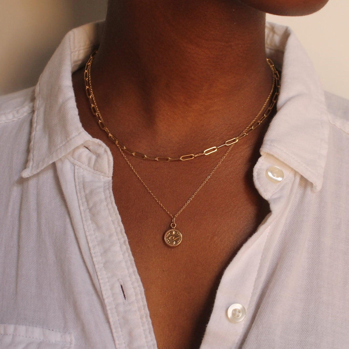 Model wearing gold elongated link necklace and gold evil eye necklace