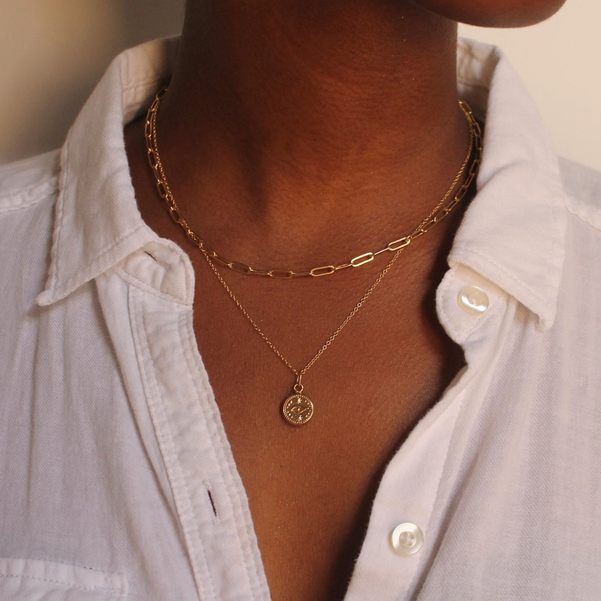 Model wearing gold elongated link necklace and gold evil eye necklace